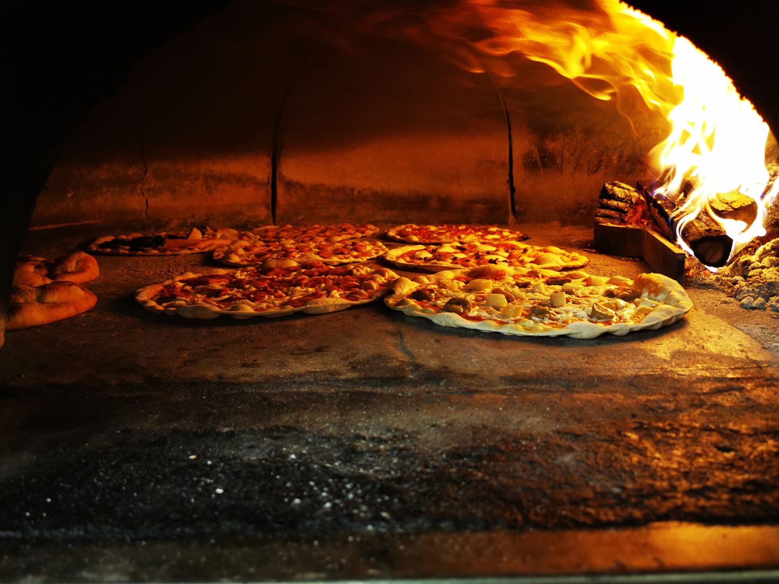 Pizze che cuociono nel forno a legna con la fiamma viva