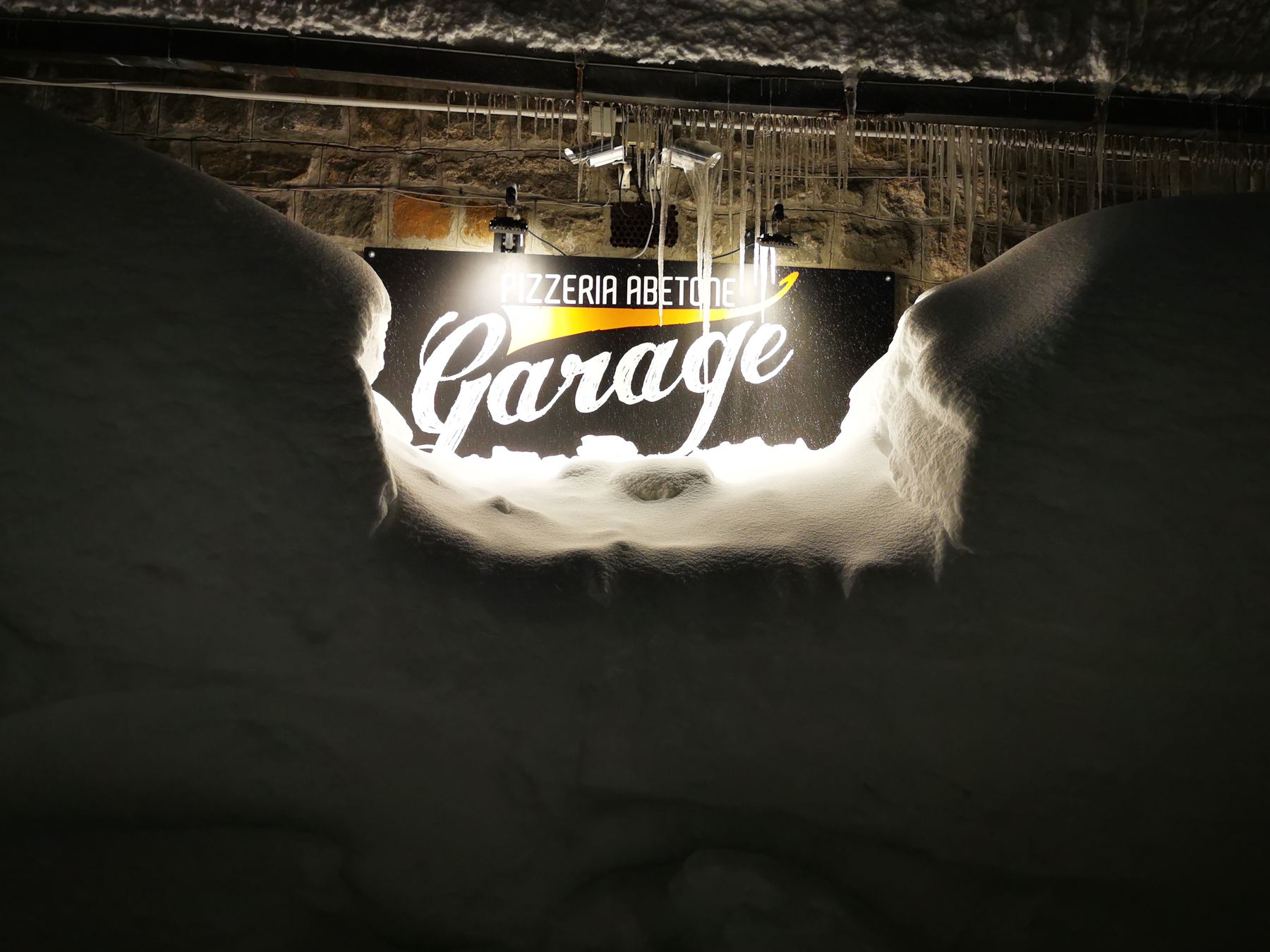 L'insegna Pizzeria Abetone Garage illuminata tra muri di neve