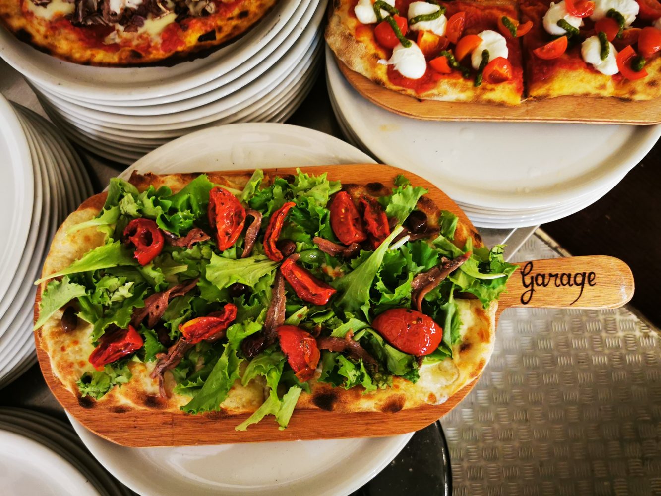 Schiacciata con rucola e pomodorini sulla pala di legno con la scritta Garage